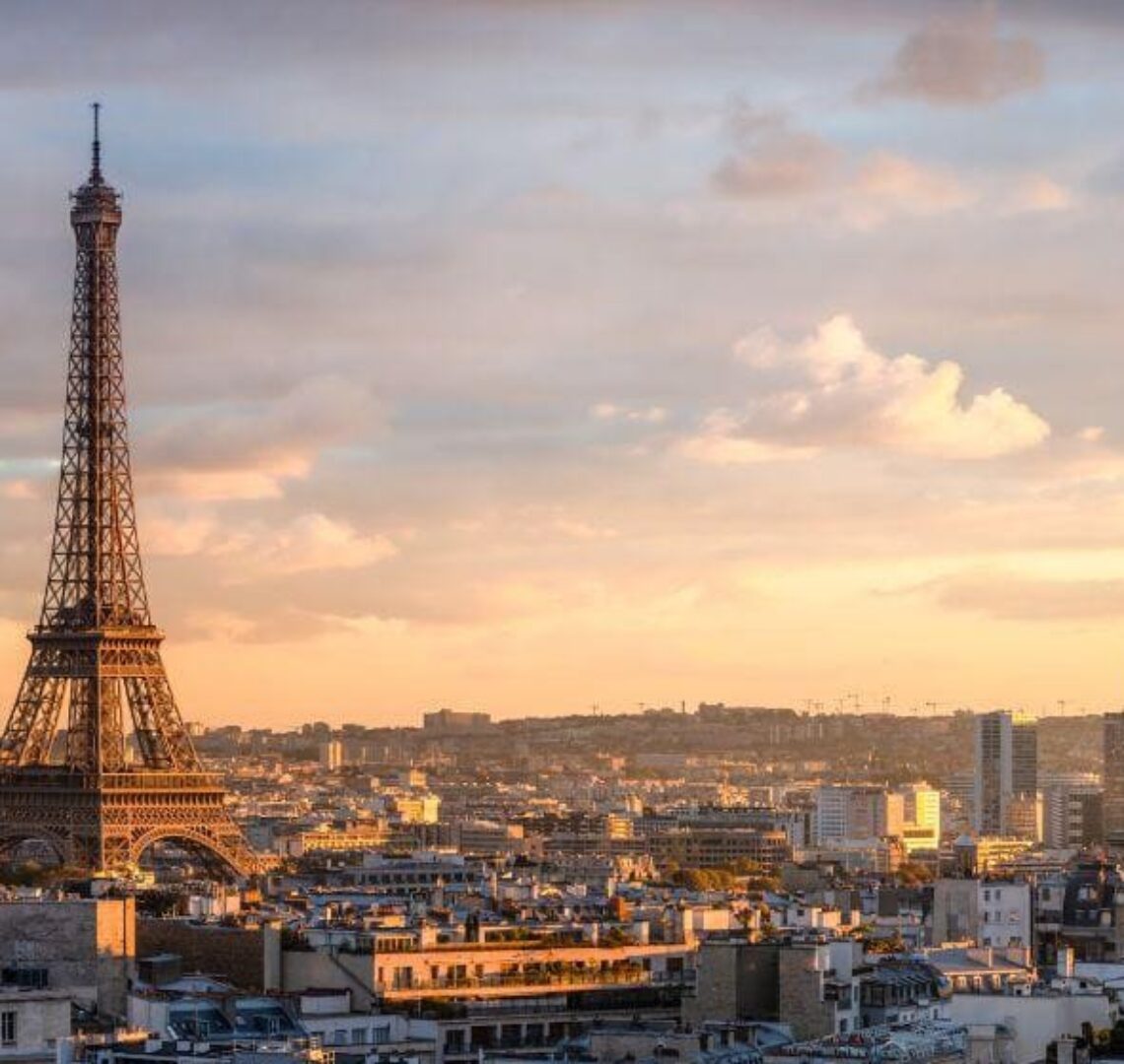 "Vue panoramique de Paris au coucher du soleil, avec la Tour Eiffel en premier plan et un vaste paysage urbain en arrière-plan."