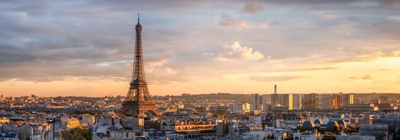 "Vue panoramique de Paris au coucher du soleil, avec la Tour Eiffel en premier plan et un vaste paysage urbain en arrière-plan."