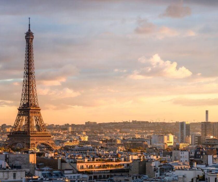 "Vue panoramique de Paris au coucher du soleil, avec la Tour Eiffel en premier plan et un vaste paysage urbain en arrière-plan."