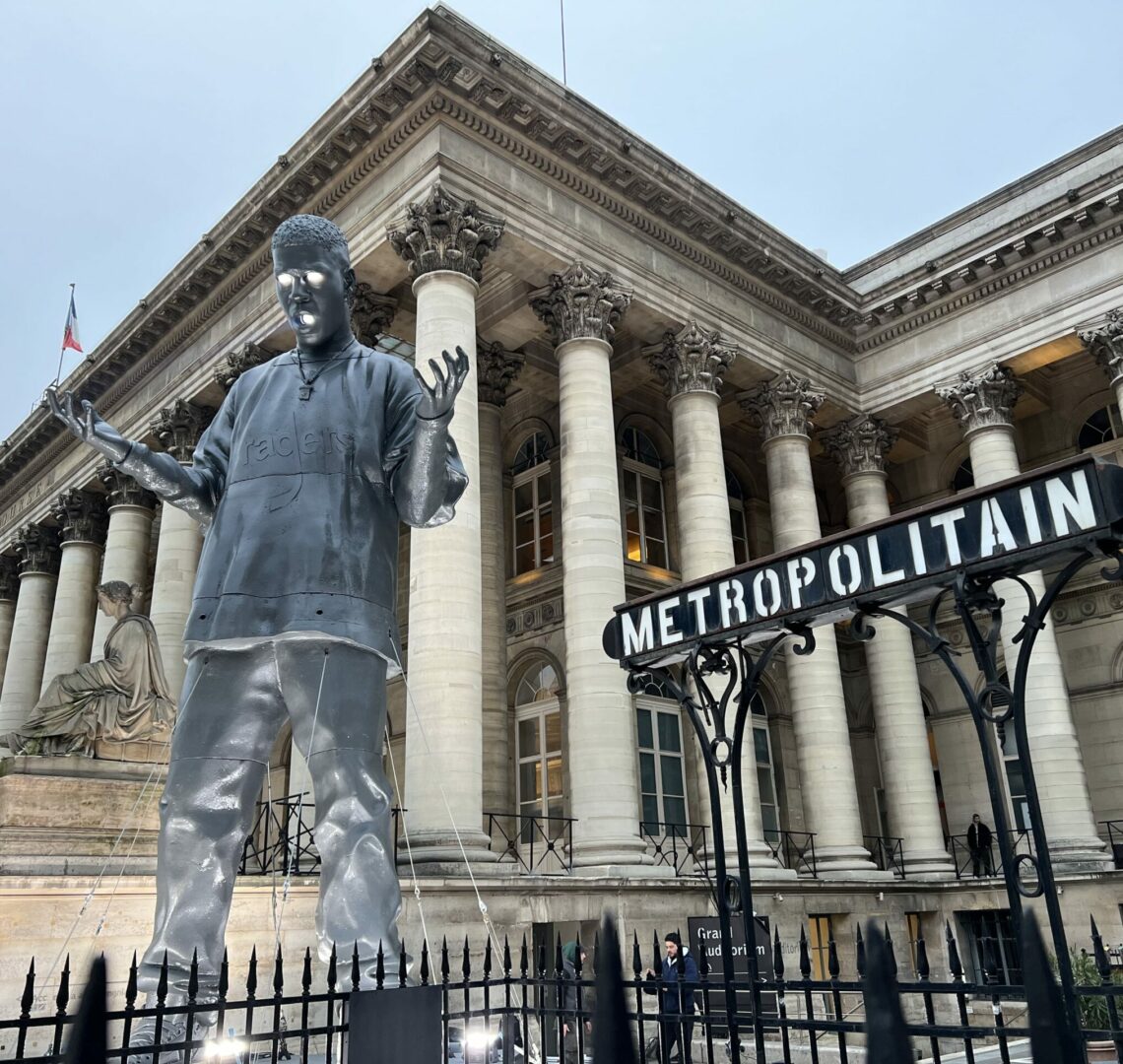 "Statue moderne devant le Palais Brongniart à Paris, avec une enseigne de métro parisien en premier plan."