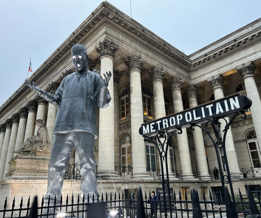 "Statue moderne devant le Palais Brongniart à Paris, avec une enseigne de métro parisien en premier plan."